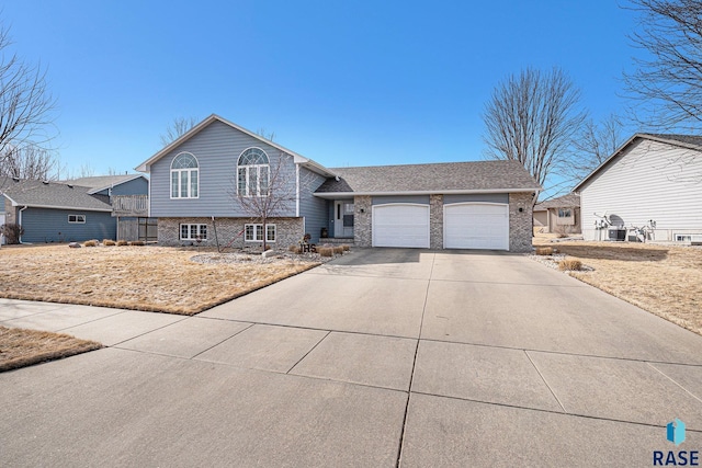 split level home featuring a garage, driveway, and brick siding