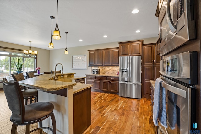 kitchen with light wood finished floors, backsplash, a kitchen bar, appliances with stainless steel finishes, and a notable chandelier