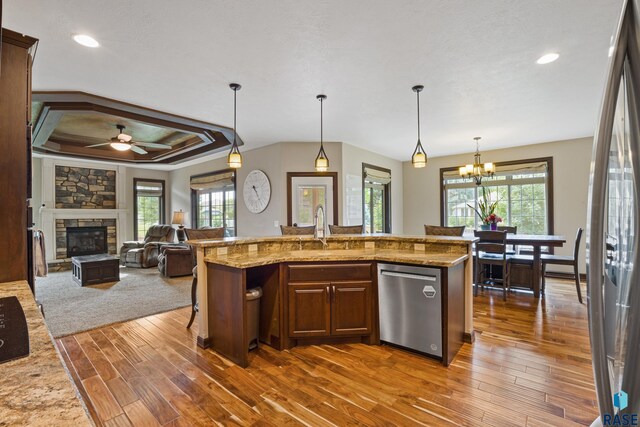 kitchen with a healthy amount of sunlight, a sink, a stone fireplace, stainless steel appliances, and ceiling fan with notable chandelier