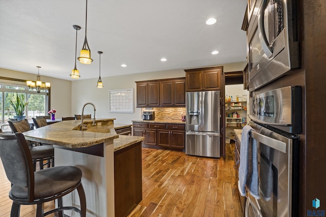 kitchen featuring a kitchen breakfast bar, wood finished floors, stainless steel appliances, an inviting chandelier, and decorative backsplash