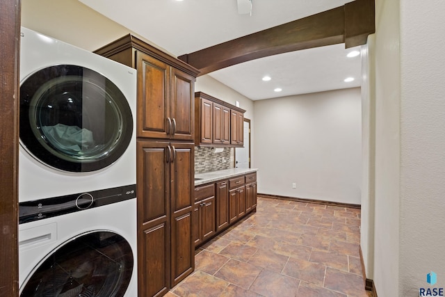 laundry area featuring stone finish flooring, baseboards, recessed lighting, cabinet space, and stacked washer / drying machine