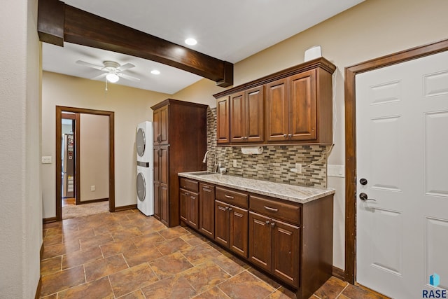 kitchen featuring beamed ceiling, stacked washer and dryer, a ceiling fan, a sink, and tasteful backsplash