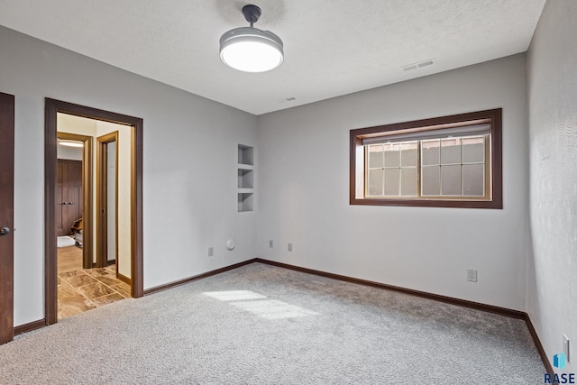 unfurnished bedroom featuring visible vents, carpet floors, a textured ceiling, and baseboards