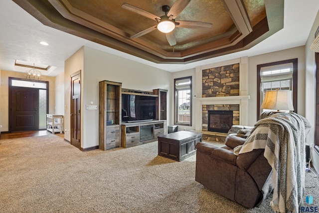carpeted living room featuring a stone fireplace, a raised ceiling, baseboards, and ceiling fan