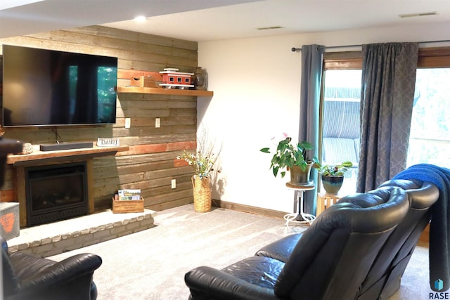 living area with visible vents, a fireplace with raised hearth, wooden walls, and carpet flooring