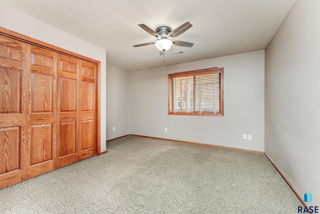 unfurnished bedroom featuring baseboards, visible vents, a ceiling fan, light colored carpet, and a textured ceiling