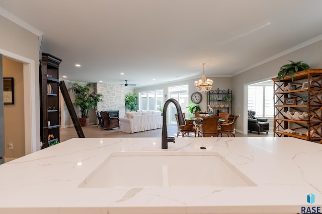 room details featuring a large fireplace, light stone counters, decorative light fixtures, crown molding, and a sink