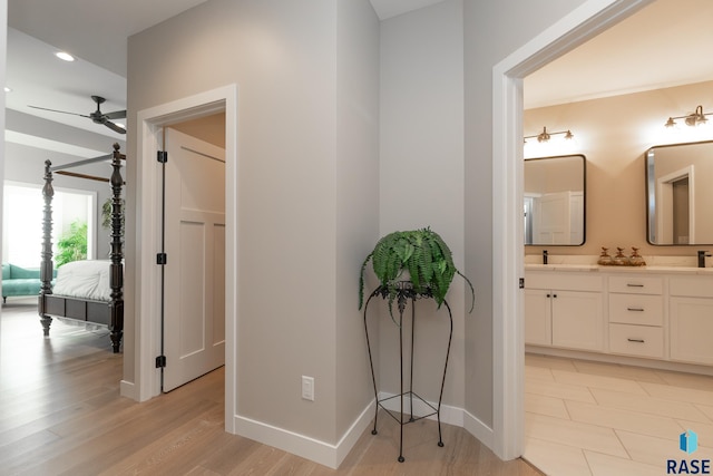 hallway featuring light wood finished floors, recessed lighting, a sink, and baseboards