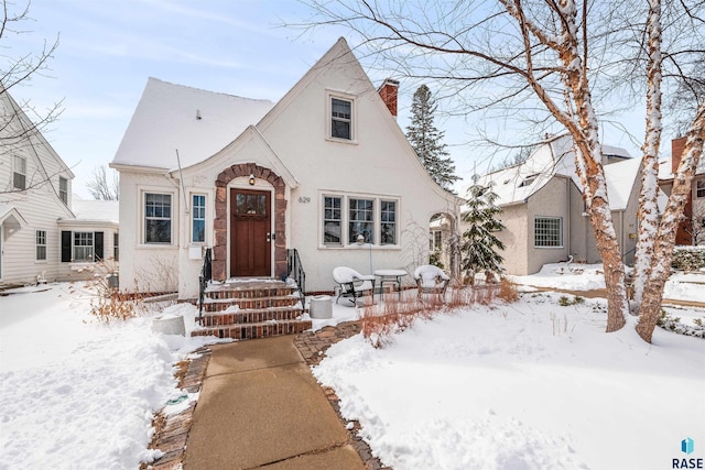 english style home with a chimney and stucco siding