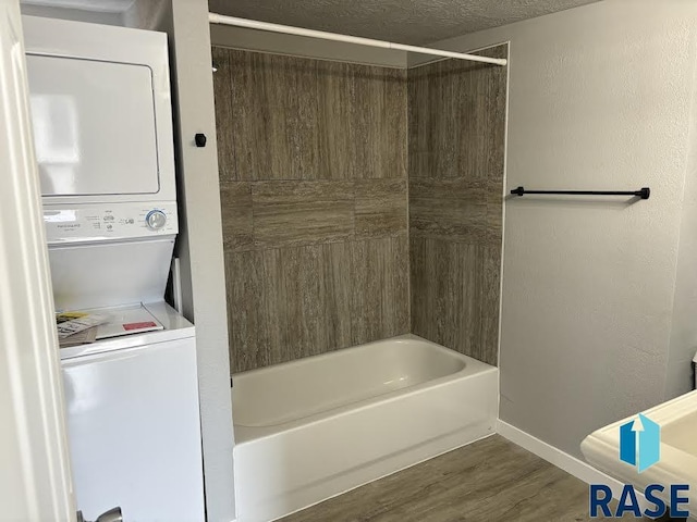 bathroom featuring stacked washer and clothes dryer, a textured ceiling, wood finished floors,  shower combination, and baseboards