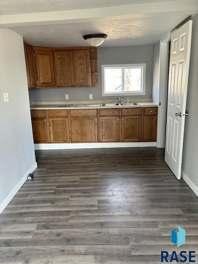 kitchen featuring dark wood-style flooring, brown cabinets, light countertops, a sink, and baseboards