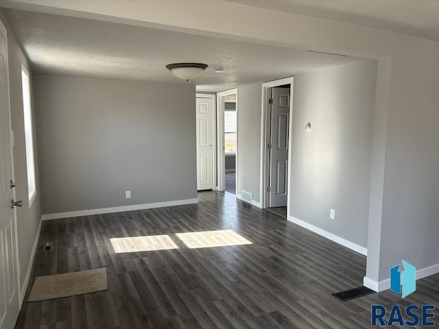 spare room with dark wood-style floors, visible vents, plenty of natural light, and baseboards