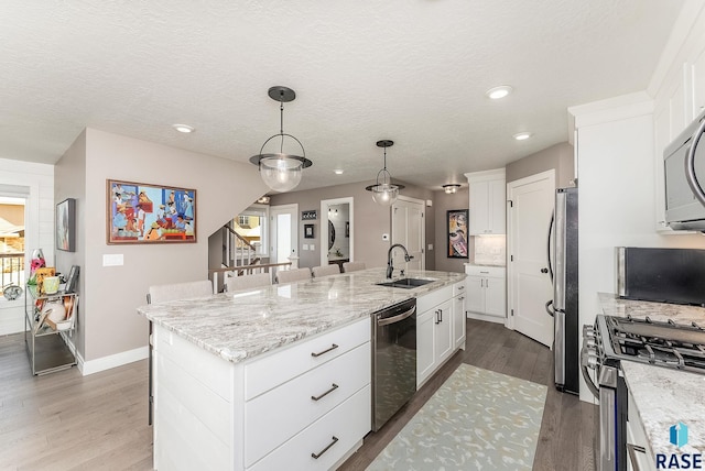 kitchen featuring a center island with sink, white cabinets, appliances with stainless steel finishes, wood finished floors, and a sink