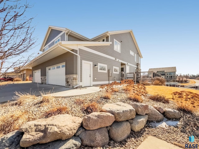 view of side of property with stone siding, driveway, a wooden deck, and an attached garage