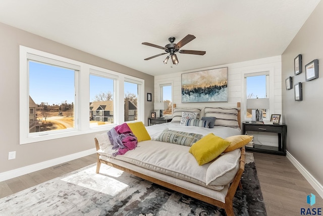 bedroom with a ceiling fan, visible vents, baseboards, and wood finished floors