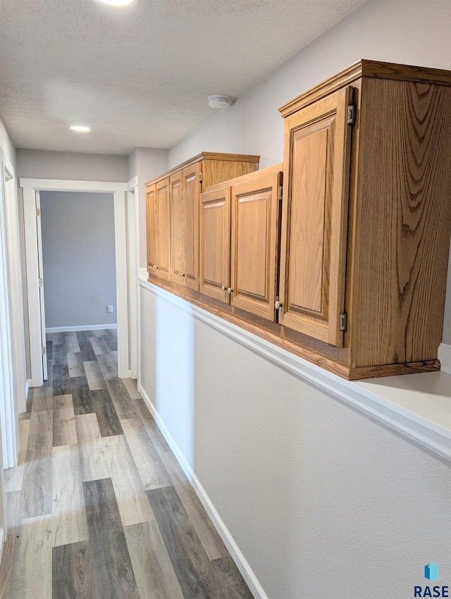 corridor featuring a textured ceiling, baseboards, and wood finished floors