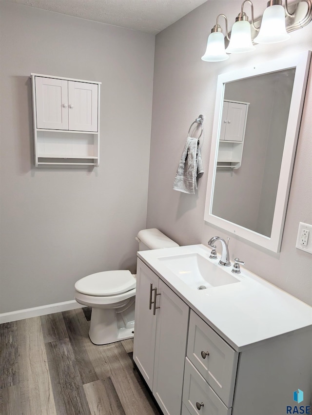 half bath with toilet, baseboards, wood finished floors, and vanity