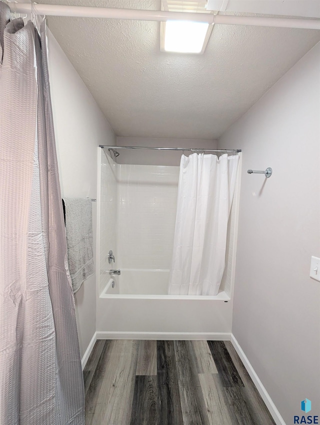 full bathroom with shower / tub combo with curtain, a textured ceiling, baseboards, and wood finished floors