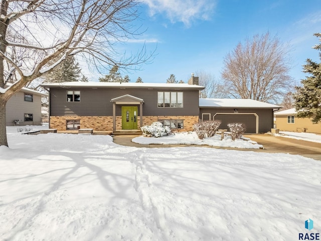 bi-level home featuring brick siding, a chimney, and a garage