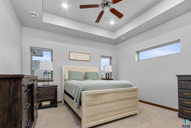 bedroom with a ceiling fan, a tray ceiling, light colored carpet, and baseboards