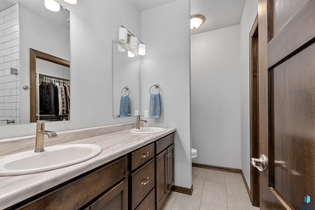 full bath featuring double vanity, toilet, baseboards, and a sink