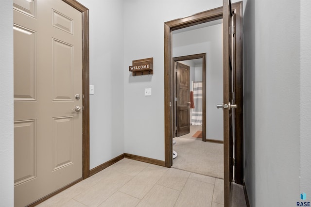 hallway featuring light colored carpet and baseboards