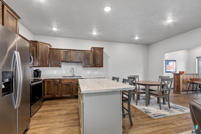 kitchen with a kitchen island, a breakfast bar, light countertops, appliances with stainless steel finishes, and a sink