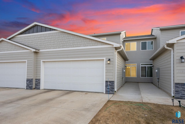 view of property with stone siding, an attached garage, concrete driveway, and board and batten siding