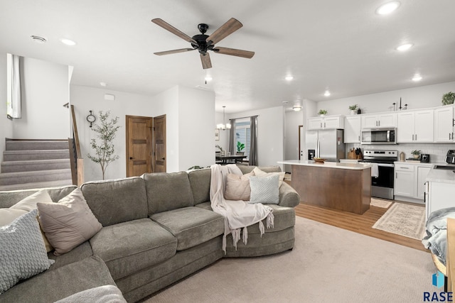 living area with light wood finished floors, stairway, recessed lighting, and ceiling fan with notable chandelier