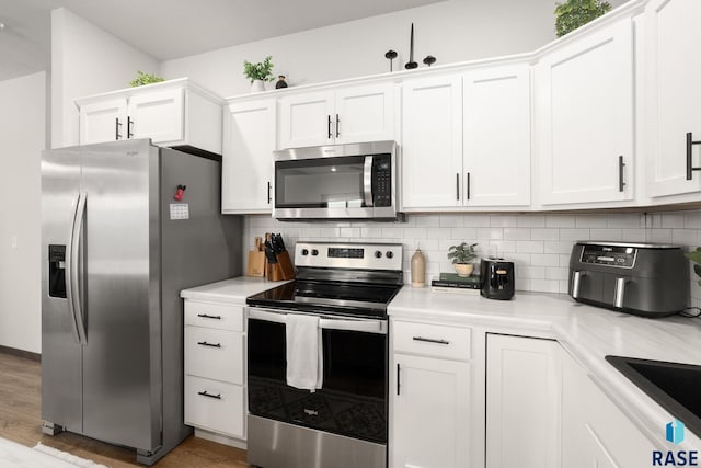 kitchen with backsplash, appliances with stainless steel finishes, white cabinets, and light countertops