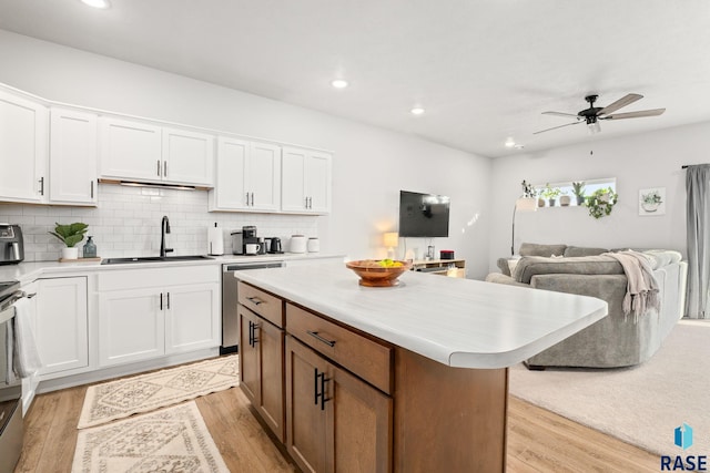 kitchen featuring open floor plan, dishwasher, light countertops, light wood-style floors, and a sink