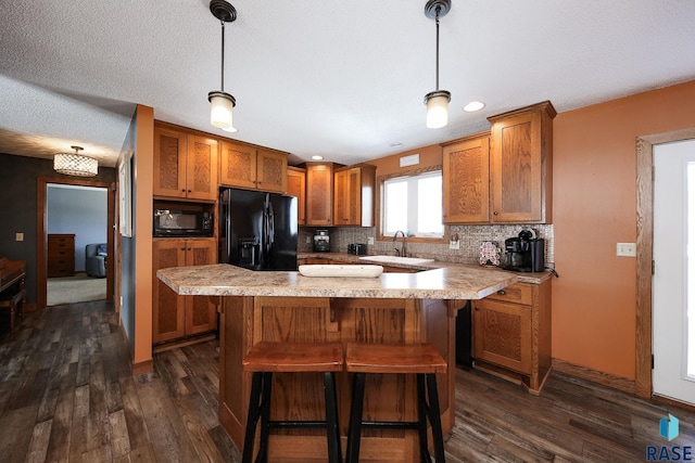 kitchen featuring black appliances, a sink, tasteful backsplash, dark wood finished floors, and brown cabinetry