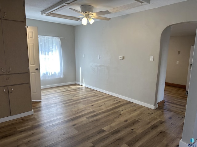 empty room featuring ceiling fan, wood finished floors, arched walkways, and baseboards