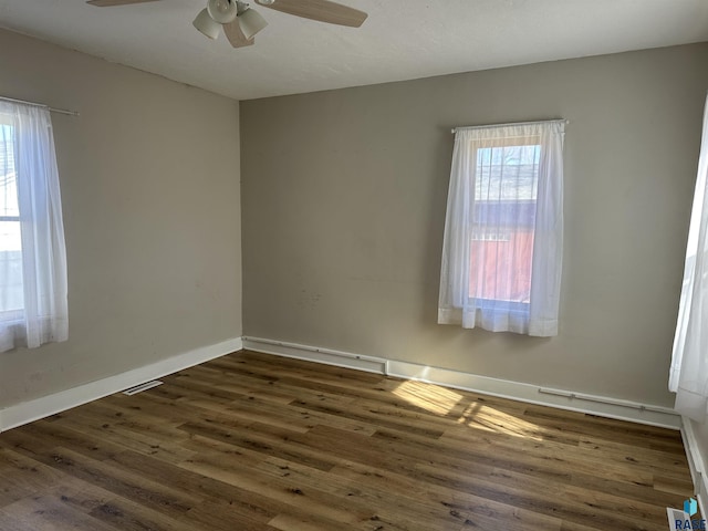 empty room with visible vents, a ceiling fan, baseboards, and wood finished floors