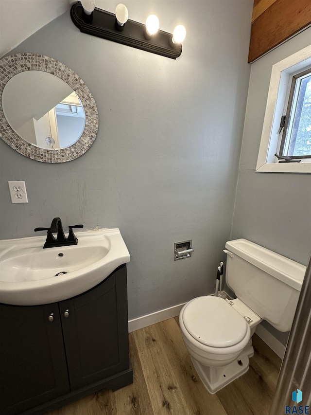 half bath with vanity, toilet, wood finished floors, and baseboards