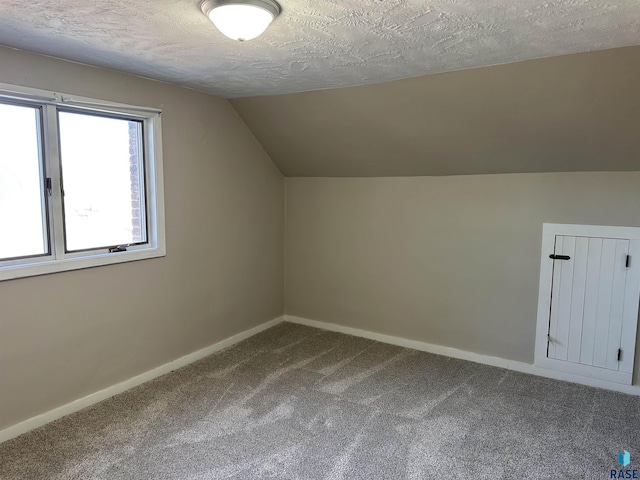 additional living space with vaulted ceiling, a textured ceiling, baseboards, and dark colored carpet