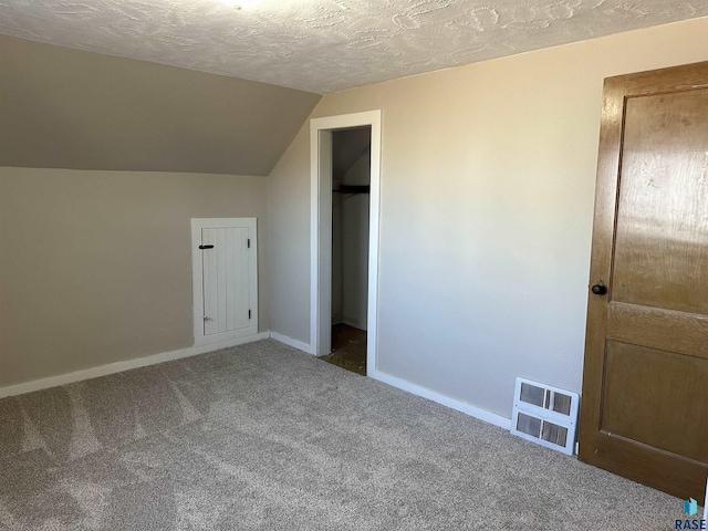 unfurnished bedroom with visible vents, baseboards, vaulted ceiling, carpet flooring, and a textured ceiling