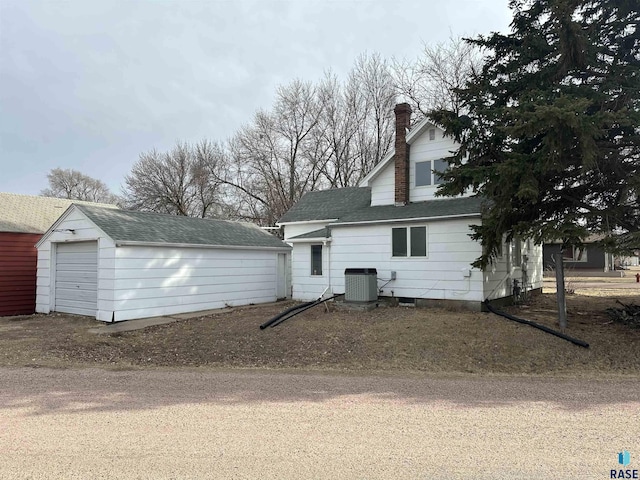 rear view of house featuring cooling unit, driveway, a chimney, an outdoor structure, and a detached garage