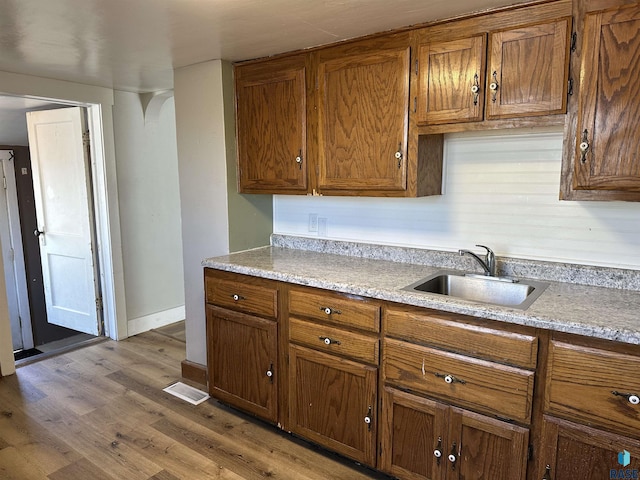 kitchen featuring baseboards, wood finished floors, brown cabinets, and a sink