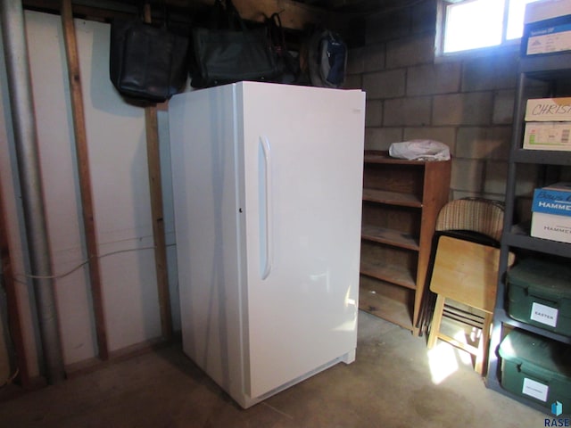 basement featuring concrete block wall and freestanding refrigerator