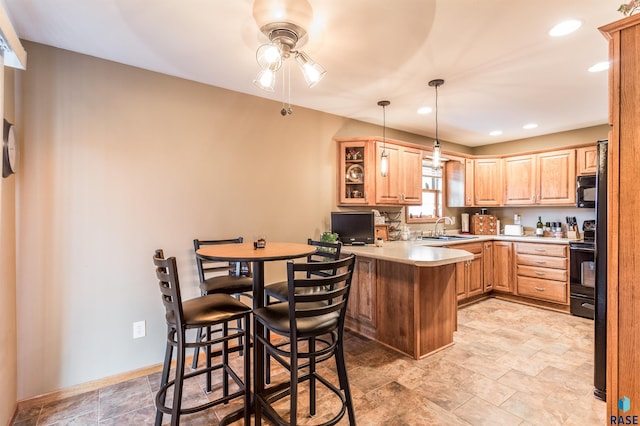 kitchen with baseboards, a peninsula, a sink, light countertops, and black appliances