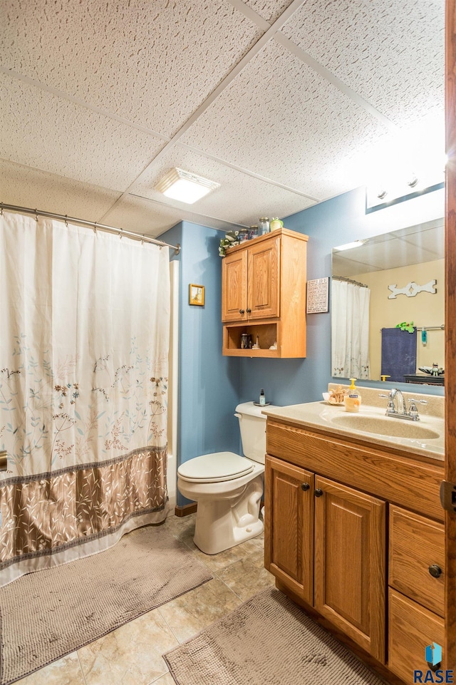 bathroom featuring a shower with shower curtain, a drop ceiling, toilet, and vanity