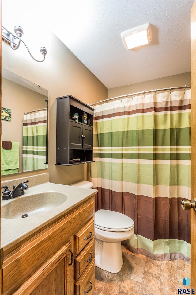 full bathroom with curtained shower, toilet, vanity, stone finish floor, and a textured ceiling