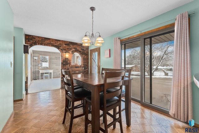 dining room featuring arched walkways, a chandelier, brick wall, and a textured ceiling