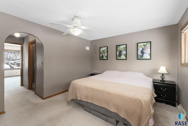 bedroom with baseboards, arched walkways, light carpet, and a ceiling fan