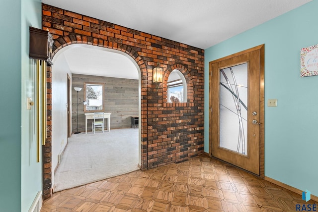 foyer entrance featuring wooden walls, baseboards, arched walkways, and brick wall