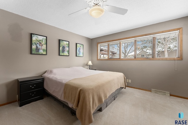 bedroom featuring light carpet, visible vents, a textured ceiling, and baseboards