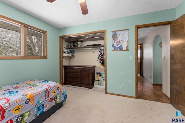 carpeted bedroom with a closet, arched walkways, a textured ceiling, and ceiling fan