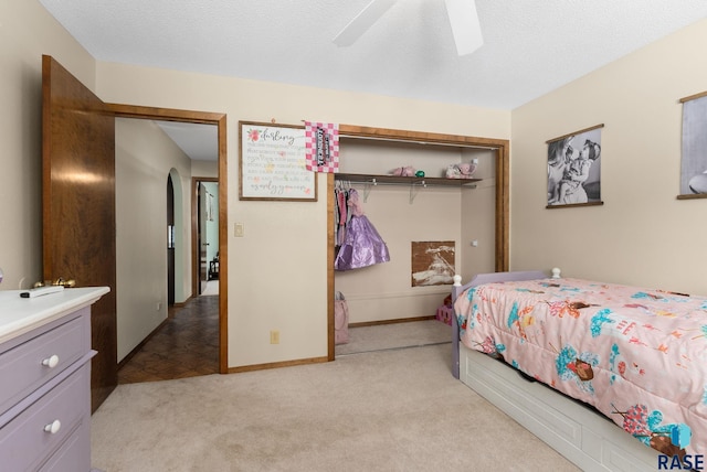 bedroom featuring a textured ceiling, arched walkways, a closet, and light carpet