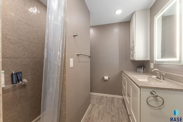 bathroom featuring a shower with shower curtain, baseboards, wood finished floors, and vanity